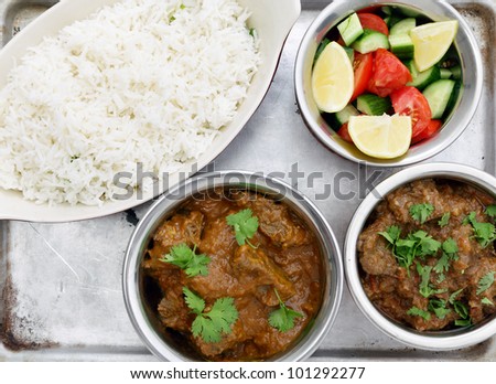 High angle view of a Madras butter beef curry (centre bottom) and ordinary curried beef with salad and rice, on an aluminium tray seen from above