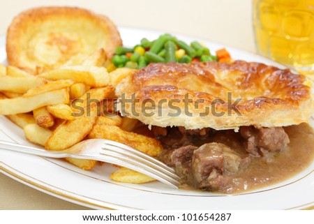 A meal of a homemade steak and kidney pie with french fried potato chips,yorkshire pudding and mixed vegetables