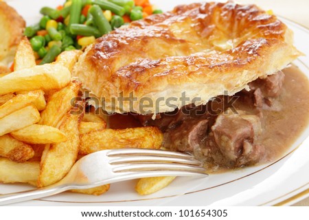 A meal of a homemade steak and kidney pie with french fried potato chips and mixed vegetables
