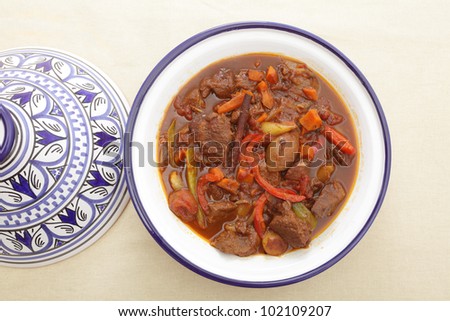 A moroccan beef tagine served in the traditional tagine dish, from above. The casserole uses beef, onion, carrots, capsicums, a cinnamon stick and a traditional mix of spices known as ras el hanout