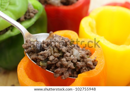 Colourful bell peppers or capsicums being stuffed with a filling of ground beef, mushroom, onion and celery.