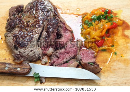A pan seared rump steak being sliced on a board with chopped pickled sweet peppers and parsley