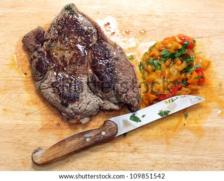 A pan seared rump steak with chopped pickled sweet peppers and chopped parsley on a wooden chopping board