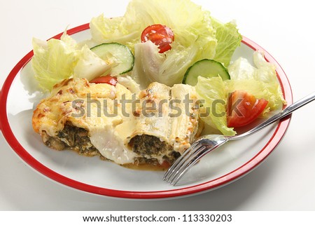 A meal of meat and spinach cannelloni with bechamel sauce served with a salad of lettuce, tomato and cucumber.