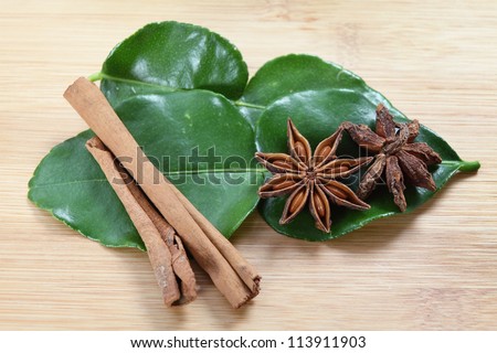 Star anise (Illicium verum - both sides of the pod shown), cinnamon and kaffir lime  (Citrus hystrix) leaves on a chopping board, these are all ingredients in Asian cookery.