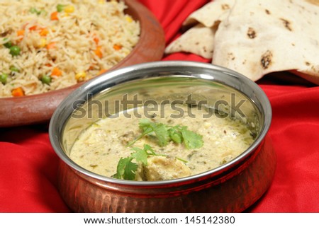 A old beaten copper serving bowl with homemade fish in green curry sauce, vegetable pilau rice on a terracotta plate and a pile of chappati indian flat breads.