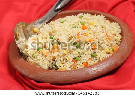 Vegetable pilau, or pulau, rice in an ethnic indian terracotta clay bowl with a rice serving spoon.