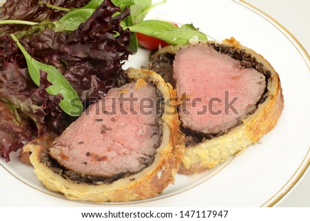 A meal of beef wellington, or boeuf en crout, served with a salad of lollo rosso lettuce, cherry tomatos and baby spinach leaves.