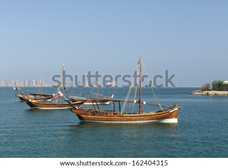 A group of small, traditional Qatari fishing dhows moored in Doha Bay, Qatar, with the towers of the Pearl residential development still under construction in the background, November 2013