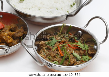 A bowl of spiced lamb curry with coriander leaves and slivers of red and green chillies, next to a bowl of Lahore-style lamb curry with split peas and some rice.