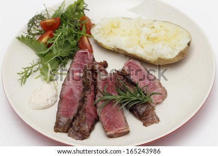 Slices of grilled gourmet wagyu rib-eye steak served with horseradish sauce, a baked potato and a fresh green salad