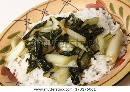 A plate with bok choi asian cabbage chopped and sauteed with sesame oil and soy sauce, served on a bed of white jasmine rice