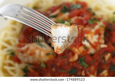 A piece of fish in arrabbiata sauce on a fork, with the spaghetti dish in the background.