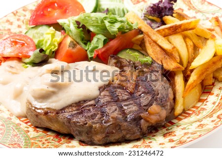 Grilled rib-eye beef steak served with mushroom sauce, salad and potato chips.