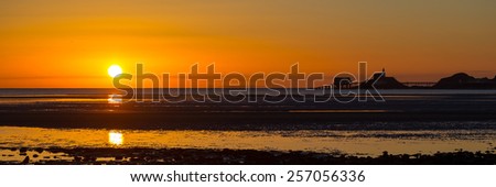 The sun rises over a wide expanse of mudflats in Swansea Bay, with the Mumbles skyline on the right.