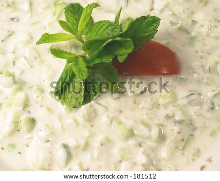 Close-up on a cucumber raita dip (cucumber in yoghourt) garnished with mint and tomato.