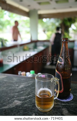 A refreshing glass of beer in a bar beside a tropical beach. Shallow depth of field to make the waiter and customer unidentifiable.