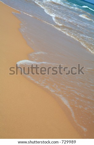 The sea washing over a tropical beach, its foam glinting in the sunshine.