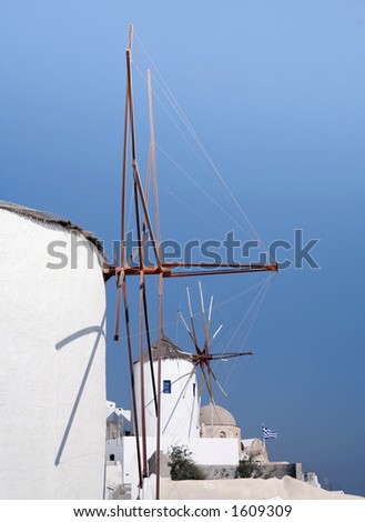 Two windmills, a church and a Greek flag at Oia, Santorini.