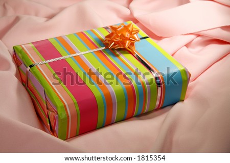 A present wrapped in pastel-striped paper on pink cloth.