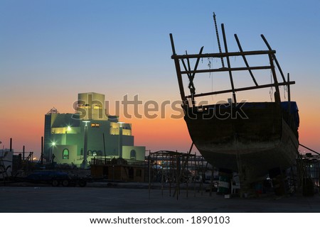 The Museum of Islamic Art, Doha, Qatar, seen from the dhow repair shipyard, with a dhow under maintenance silhouetted against the sunrise.