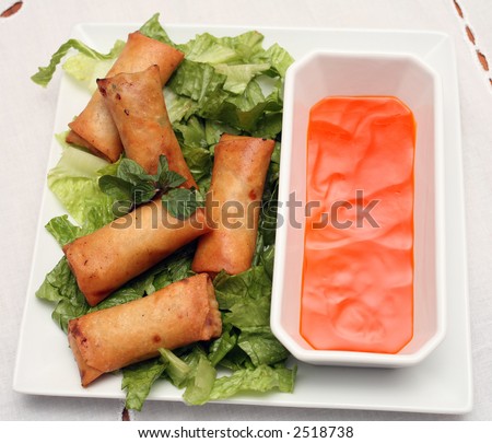 A plate of spring rolls on a bed of salad with a sweet and sour dip, on a tablecloth.