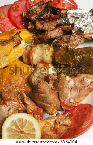 A gourmet platter of Arabian style baked lamb and chicken, stuffed vine leaves, tiny roasted potatoes and grilled lamb chops, garnished with sliced tomato and lemon.