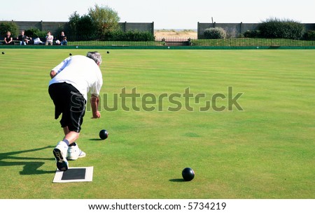 A bowler playing on the village green. Bowls is a traditional British game. The faces of the spectators are unrecognisable.