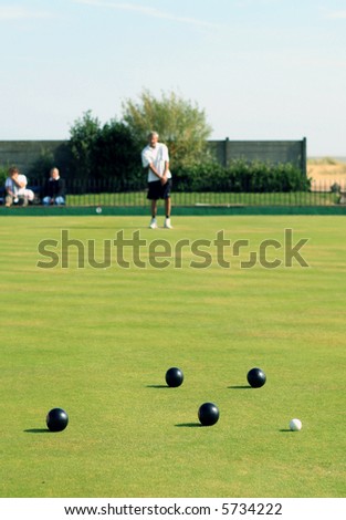 A bowler playing on the village green. Bowls is a traditional British game. The faces of the bowler and the spectators are unrecognisable, as the shallow focus is on the balls.