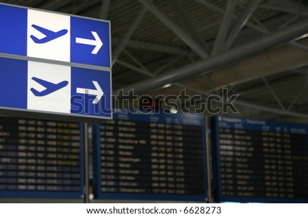 Direction arrows and out-of-focus flight information boards at a busy international airport.