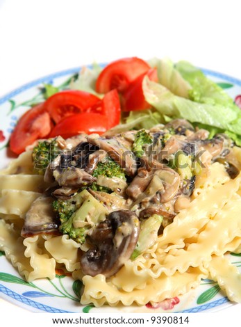 A vegetarian pasta meal of mushrooms, garlic, broccoli and onion, cooked in a cream sauce and served with tomato and lettuce salad on a bed of mafaldine (ribbon-shaped) pasta