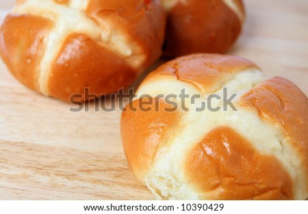 Three hot cross buns on a breadboard. The sweet breads are a traditional British favourite, especially at Easter.