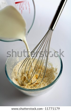 Pouring milk into a mixture of flour and eggs to make a batter for pancakes, crepes or yorkshire pudding