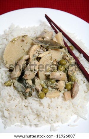 A plate of Thai green curry with chicken, bamboo shoots, kaffir lime leaves, chopped coriander (cilantro) and peas in a coconut milk curry sauce, served with basmati rice.