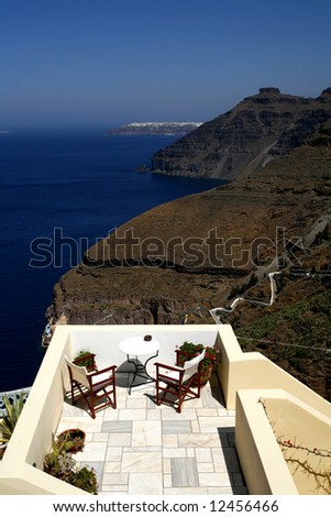 A balcony in Fira, Santorini, with a view of the dark volcanic cliffs, the steps to the harbour, the cable car and the sea in the caldera of the Cycladic island.