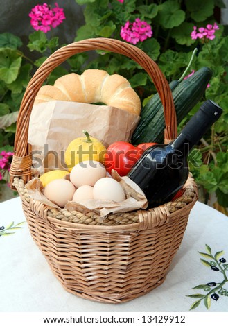 Main ingredients of the famously healthy Cretan diet - eggs, lemon,bread, wine, tomatoes and cucumber - in a basket with geraniums behind. The bottle reflects the courtyard of a Cretan stone house.