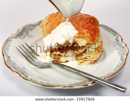 A puff pastry Apple turnover on a plate with cream being poured over it