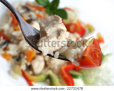 Chicken risotto on a fork with a piece of tomato, the meal out of focus in the background.