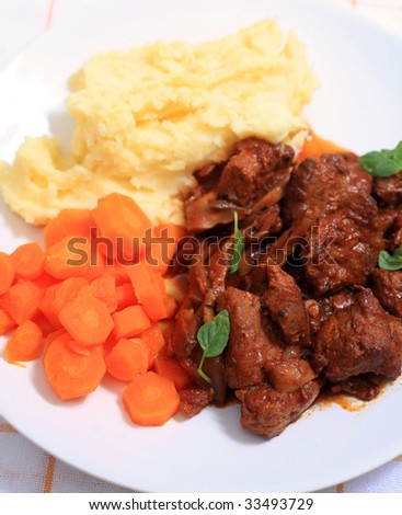 A meal of boeuf bourguignonne French beef stew served with creamed mashed potatoes and sliced carrots and sprinkled with fresh mint leaves.