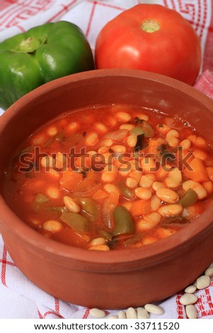 A terracotta serving bowl of traditional Greek white bean soup. with tomato and capsicum and dried white beans, which are among the main ingredients, along with olive oil, celery, carrot and onion.