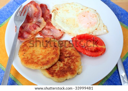 A fried breakfast of potato pancakes, bacon, egg and tomato.