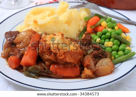 Close-up on a meal of beef and onion stew with parsley dumplings, served with boiled, mashed potatoes and mixed vegetables.