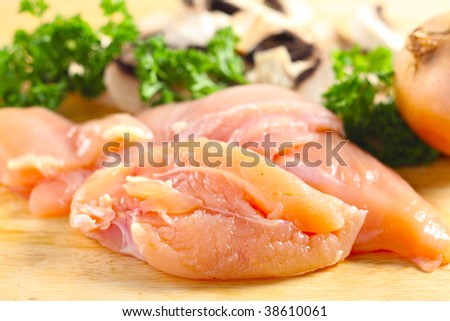 The ingredients for a chicken and mushroom dish, chicken breasts, sliced mushrooms, onion and parsley, on a chopping board, side view, shallow depth of field