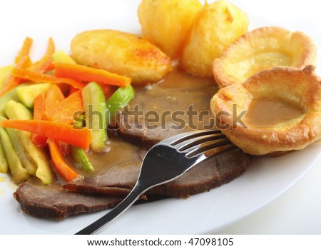 Traditional british meal of roast beef and yorkshire pudding (popovers) served with roasted potatoes and julienned sauteed carrots and courgettes, with plenty of gravy.