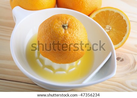 Half an orange in the process of being squeezed into a china juicer, with other oranges behind over a white board.