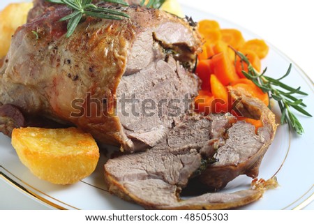 A serving plate with a joint of roasted boneless lamb roasted potatoes and boiled carrots, garnished with sprigs of rosemary