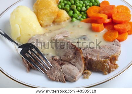 A meal of roast lamb with roasted potatoes, boiled peas and boiled sliced carrots with a fork