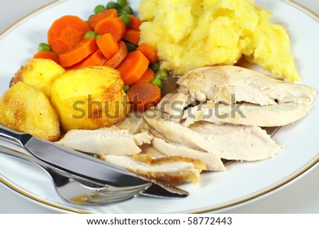Close-up view of a roast chicken dinner and cutlery, comprising sliced chicken breast, roast potatoes, mixed vegetables, mashed potato and gravy