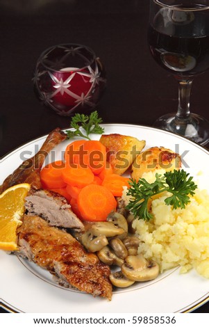 A romantic candle-lit dinner of roast duck, potatoes, mushrooms and carrots on a dark wooden table.