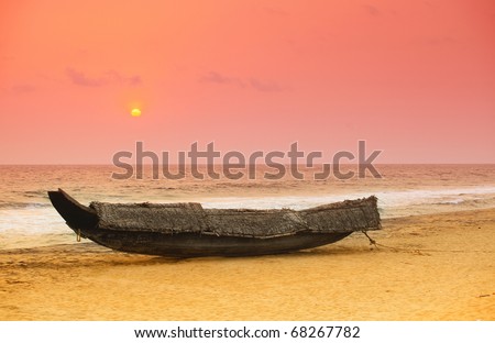 The sun sets behind a beached traditional Kerala, India, fishing boat. The boat has been covered with coconut palm thatch as a protection against the weather.
